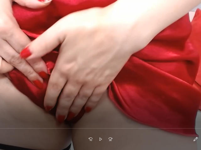 PriscillaHotMature's hands with red nails, pulling up her red dress, exposing her pussy. Her fingers gently grasp the fabric, showing her pale skin.