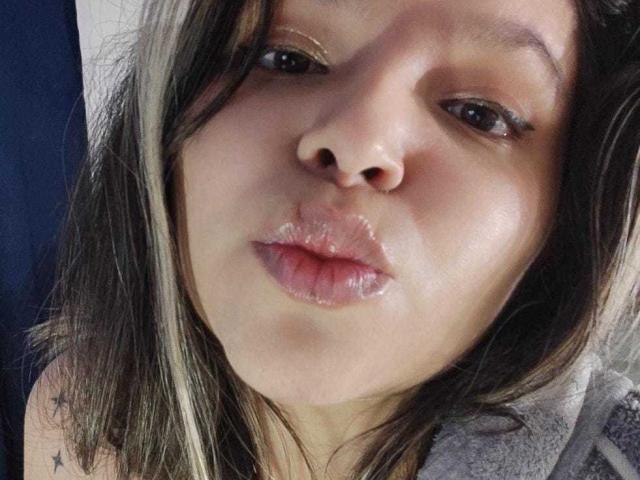 Myalewwis with puffy, shiny lips making a kissy face, her brown eyes half-open, wearing subtle makeup, and showing a star tattoo on her right shoulder.