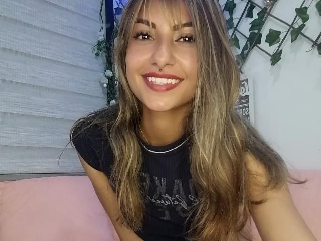 LucianaDeivys ha lunghi capelli castani, un piercing al naso ed è sorridente, con il rossetto rosa. Indossa una maglietta nera e una sottile collana, mettendo in risalto il suo viso carino..