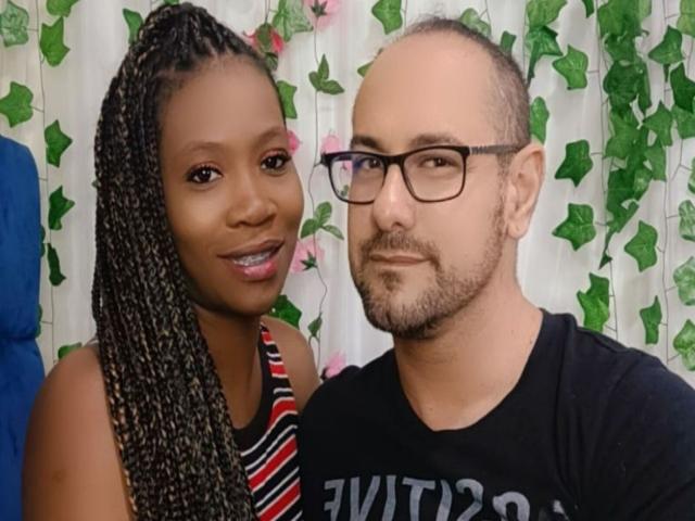MaxAndMegan69 tiene la piel oscura, cabello largo trenzado y senos pequeños. Está sonriendo, junto a MaxAndMegan69, que es calvo, lleva gafas, tiene barba y una camisa negra..