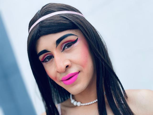 Catalina Castro heeft lang zwart haar, roze lippenstift, opvallende roze en rode oogmake-up, een parelketting en een roze hoofdband. Haar borsten zijn klein, haar achterkant is niet te zien..