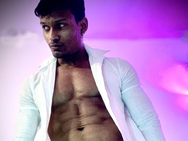 JacksonCooper with a toned, muscular chest, wearing an open white shirt, has short black hair, a small earring, and a serious expression, illuminated by purple and pink light.