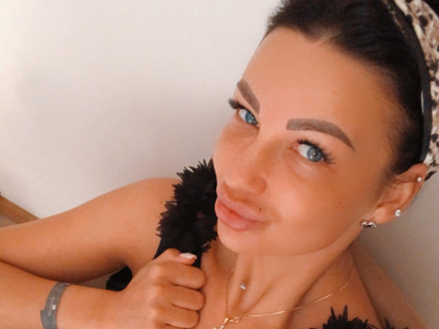 Kristen Stark, con gli occhi azzurri, i capelli scuri e una fascia per capelli con stampa leopardo, che tiene una piuma nera, indossa orecchini e una collana, sorride leggermente e ha un braccialetto al polso..