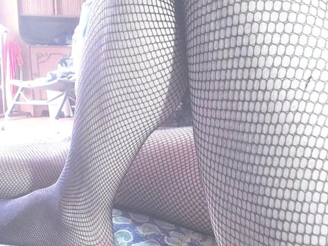 Sweetpenis's legs in black fishnet stockings, showing a pattern of hexagonal holes. One leg is crossed over the other, creating a slightly tangled look.