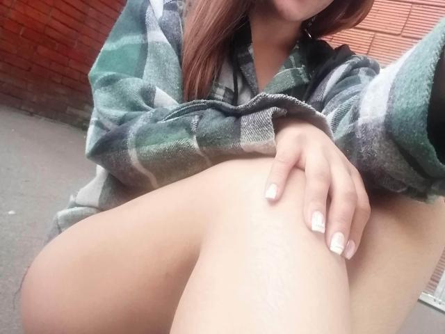 A camisa xadrez verde e cinza de TamyParist, com ela agachada e a mão na coxa, exibindo suas unhas pintadas de branco e a perna nua, sem calças, apenas sua pele brilhante..