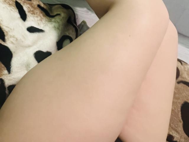Barbarica's pale, smooth thighs are crossed, showing her bare, soft ass. A fuzzy, leopard-print blanket is partially visible in the background.