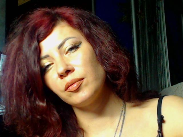 JuliaIce tiene el pelo rojo ondulado, ojos marrones y usa delineador de ojos oscuro con pestañas largas. Está mirando hacia abajo con una expresión de puchero, mostrando sus labios y un piercing en la nariz..