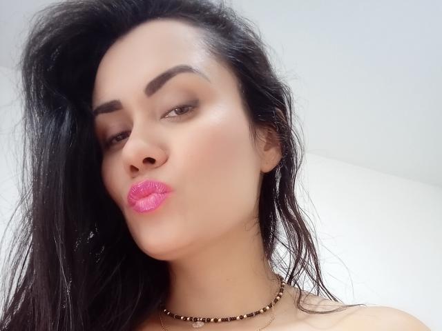 XBellaEvaX has pink lipstick, dark eyebrows, and wet black hair, pouting her glossy lips. She's wearing a black bead necklace and has a light skin tone.