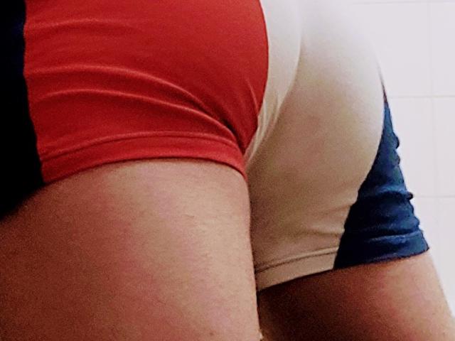 Oli69's butt in tight, red-white-blue shorts, showing a curve of his ass and a bit of his thigh. Skin is light with some hair visible.