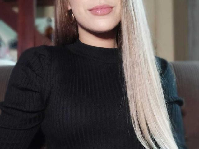 MartinaLimax tem cabelos loiros longos, um suéter preto texturizado e lábios rosados. Seus pequenos seios mal são visíveis, e ela está usando brincos de ouro..