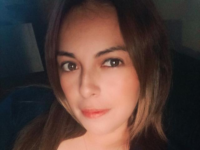 Seher has light brown eyes, subtle makeup, and a slight smile. She's looking directly at the camera with medium-length brown hair. Her tits are not visible.