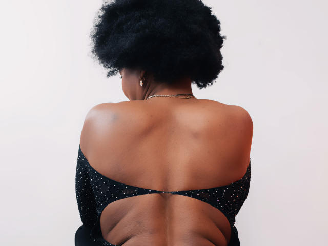 Camila Sandovali ha la schiena rivolta verso la telecamera, mostrando la sua pelle scura e liscia e i suoi grandi capelli afro. Indossa una maglietta nera, scintillante, con le spalle scoperte..