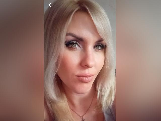 A loira Alisa, com lábios carnudos, olhos verdes e delineador marcante, veste uma blusa rosa, tem um rosto bonito e está fazendo uma carinha de beijo. Seus seios são pequenos..