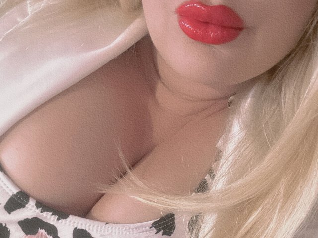 Los grandes senos de RoseStaar, su escote y sus labios rojos brillantes. Tiene el pelo rubio, una camisa blanca y una blusa con un estampado blanco y negro, que realza su pecho generoso..