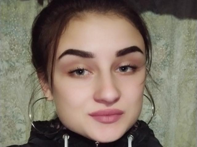 Het gezicht van LisaViv, ze heeft dikke, donkere wenkbrauwen, groene ogen en roze lippenstift. Ze draagt een zwarte capuchon met grote zilveren oorringen. Haar bruine haar is naar achteren gebonden..