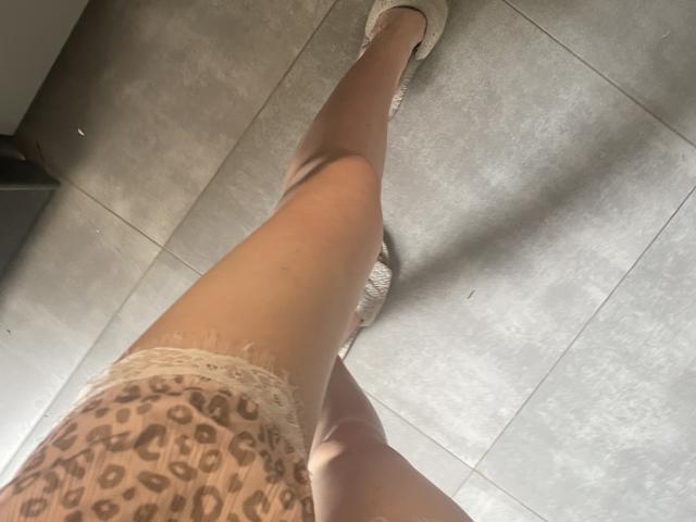 La gamba di RozalinaPleasure, estesa verso l'alto, indossa pantaloncini leopardati con bordi in pizzo bianco e scarpe da ginnastica bianche, su un pavimento piastrellato grigio. La sua pelle è chiara e la foto è scattata dal basso..