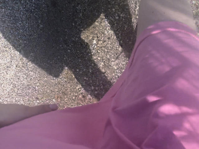 RozalinaPleasure's pink dress, her hand on the ground, and a dark shadow on textured gravel. Her dress has a soft, flowing texture, and her hand is slightly visible.