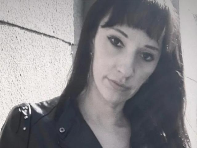 A MissieLorrie tem cabelo castanho escuro com franja, delineador preto e um sorriso discreto. Ela está vestindo uma jaqueta de couro preta com ombros abotoados. Ela tem seios pequenos..