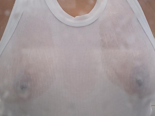 MatureJennyX's white, ribbed tank top is sheer, revealing her small, perky tits with visible nipples through the fabric. Her chest is centered in the image.