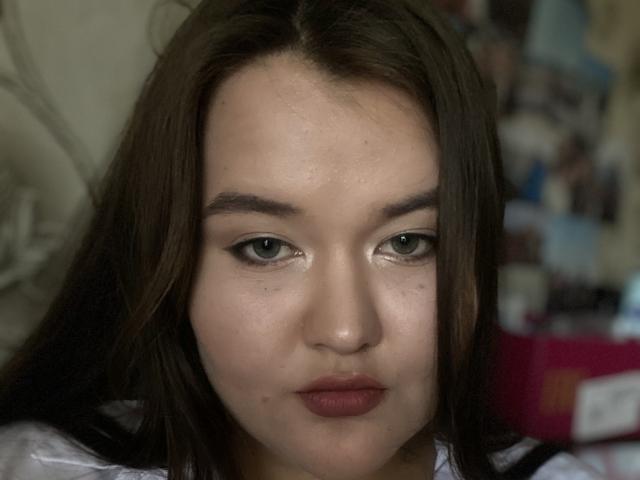 IsadoraStefanie tiene piel clara, ojos marrones y cabello lacio castaño, con un maquillaje sutil y lápiz labial rojo, mirando directamente a la cámara con una expresión neutra..