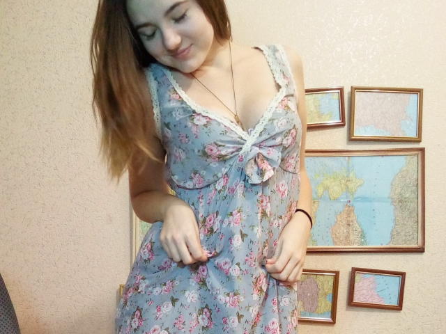 NonStop with light brown hair, wearing a floral dress with lace trim, looking down, hands on dress, showing small tits, light skin, subtle smile, necklace, wall with maps.