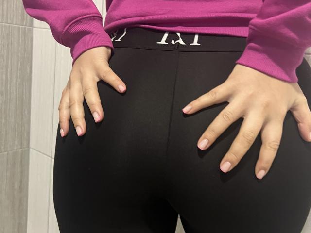 Barbarica's hands on her black ass, wearing black leggings, pink sweatshirt, with pink nails, in a tiled room.