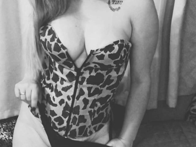 OliviaMara indossa un corpetto senza spalline con stampa leopardo, con zip frontale, che mette in mostra il suo seno grande e formoso, con lunghi capelli ondulati e un tatuaggio sulla spalla destra, e indossa biancheria intima nera..