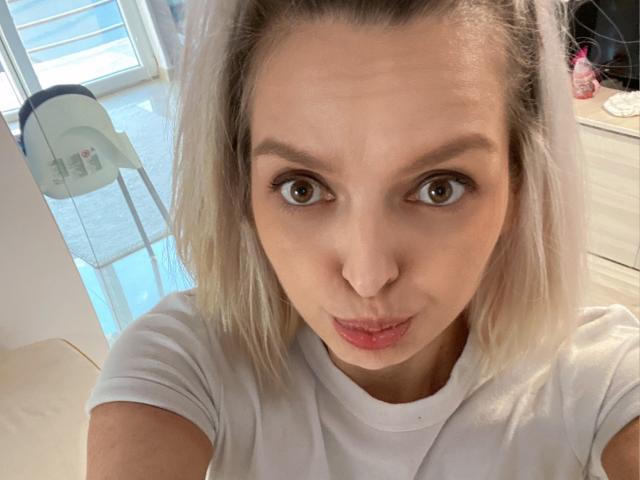 DouceAmelia with pouty lips, blonde bob, brown eyes, white shirt, looking at camera, small nose, soft light, casual selfie, indoors, light skin, cute, slightly annoyed expression.