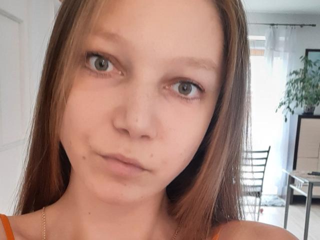 LovelyxEmilly heeft een bleke huid, groene ogen en lichtbruin haar. Ze draagt een oranje top met een gouden ketting en heeft kleine sproeten op haar gezicht..