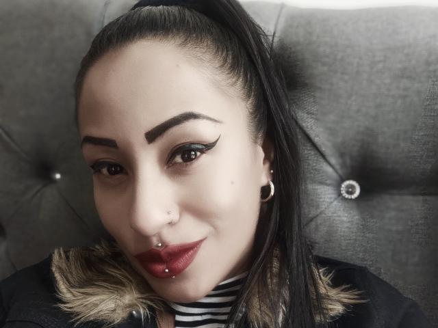 LunaCandy a des sourcils foncés, une longue queue de cheval noire, du rouge à lèvres, un anneau au nez, un piercing aux lèvres et des bouchons d'oreille noirs. Elle porte une chemise rayée avec une veste bordée de fourrure..