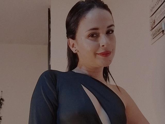 Wendy Schultz, com cabelo escuro, batom vermelho e um vestido preto com recortes, que mostra seu ombro nu e parte do seio, sorrindo levemente..
