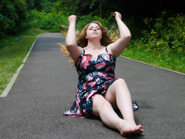 JessikaDaniels, with her tits up, arms raised, sitting on a road, legs spread, wearing a floral dress, blonde hair flying, bare feet, looking happy and relaxed.