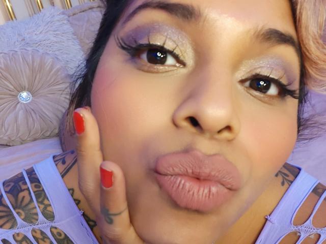 Chili's giving a close-up footjob with her glossy red nails and plump lips puckered, her tattoos visible on her shoulders.