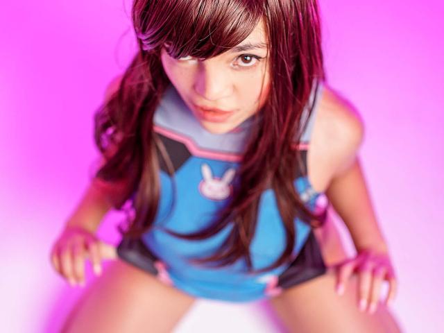 DreamySweetLucy con lunghi capelli castani, abito blu e rosa, logo a forma di coniglio, che guarda verso l'alto, mani sulle ginocchia, illuminazione rosa e viola, messa a fuoco morbida, sexy, carina, femminile, attraente..