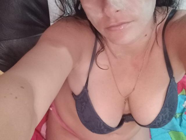 AmberDemons with red curly hair, lying on a bed, legs up, showing yellow and pink painted toenails, feet in focus, wearing a white shirt, black headboard, red blanket.