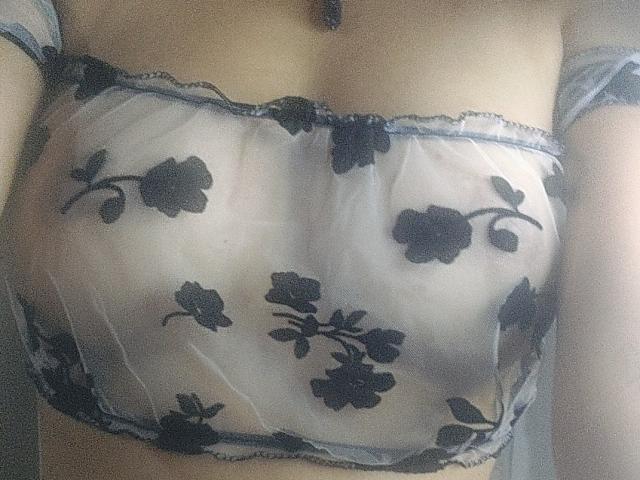 RosalieBlacks durchsichtiger BH mit schwarzer Blumenstickerei, der ihre Brüste zeigt, aus leichtem Stoff und mit schwarzen Trägern, in weichem, natürlichem Licht. Ihre Haut ist blass und glatt..