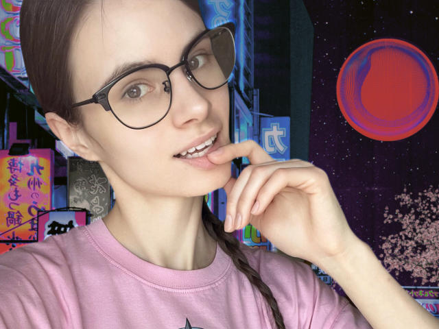 BatSama met een bril, een roze shirt, gevlochten bruin haar, die haar lippen aanraakt, waarbij haar kleine borsten zichtbaar zijn, met een lichte huid en een schattende, sexy glimlach. Stedse neonachtergrond met een rode cirkel..