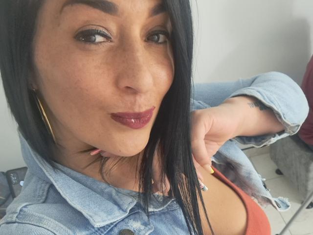 Karen e Scott: Ela tem olhos castanho-escuros, lábios vermelhos brilhantes, cabelo preto e liso, veste uma jaqueta jeans e uma blusa vermelha, com uma expressão levemente emburrada, com uma mão perto do peito..