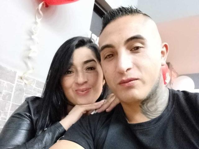 Karen e Scott: Ela tem seios grandes e está sorrindo, tem cabelo preto. Ele está olhando para a câmera, tem um corte de cabelo curto e um tatuagem no pescoço, ambos estão vestindo camisas pretas..