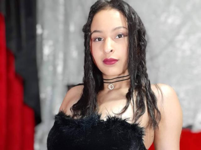 MartinaMar with black braided hair, red lipstick, black choker with ring, black furry strap dress, looking at camera, medium skin, small tits, subtle makeup, serious expression.
