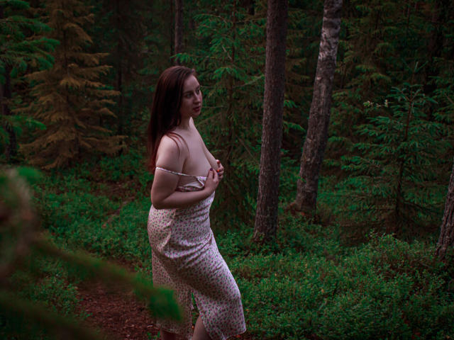 ViaLattea with pale skin and dark brown hair in a floral dress, holding her tits, standing in a forest, looking to the side with a slightly open mouth.
