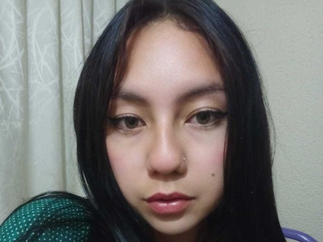 VeroHotLove tiene el pelo largo y negro, un piercing en la nariz y una pequeña peca en la mejilla. Está mirando directamente a la cámara con los labios ligeramente entreabiertos y de color rosa..