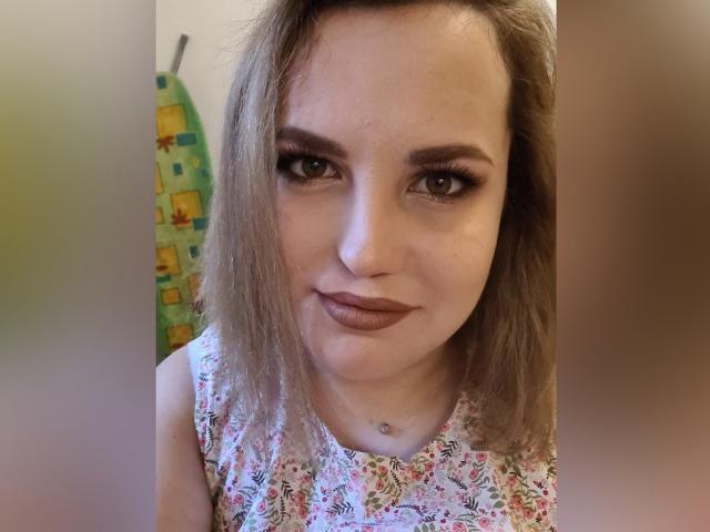 VladaCandy tiene el cabello castaño claro, cejas pobladas y usa lápiz labial oscuro. Está mirando a la cámara con una ligera sonrisa, y lleva puesto un top floral sin mangas..