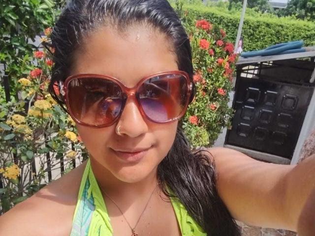 BrunetteLiaSex with wet dark hair, wearing red sunglasses, nose ring, and green halter top, showing a slight smile. Her boobs are not visible. She's taking a selfie.