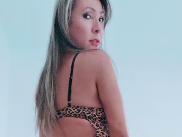 Camila Mancini mit langem, blondem Haar, die nach hinten schaut, trägt einen BH mit Leopardenmuster, zeigt ihren nackten Rücken und ist leicht gedreht, um ihre kleinen, prallen Brüste zu zeigen..
