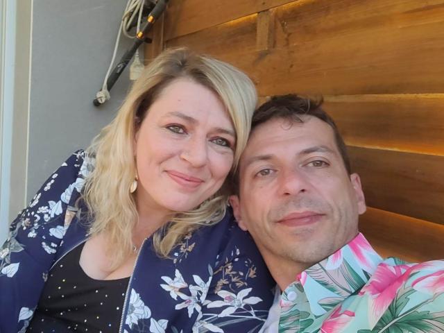 OscarBella has blonde hair, blue floral jacket, and smiling at camera. OscarBella, with brown hair, floral shirt, and smiling, stands next to her. Both have cute faces.