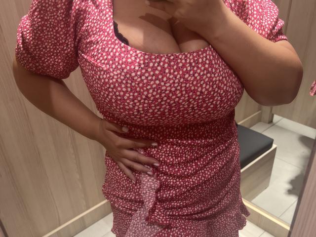 Les grandes seins de Barbarica dans une robe rouge et blanche, dévoilant sa poitrine avec de la dentelle noire, une main sur la hanche, autoportrait pris dans un miroir, pièce à lambris, téléphone à la main, peau brune..