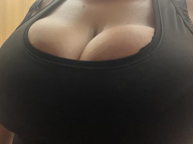 Barbarica's big tits in a black tank top, showing plenty of cleavage with her chest pressed together. Her skin is light brown, and the top has a lace trim.