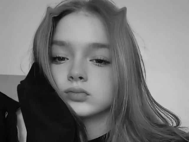 LaPochka tiene el cabello claro y ondulado, y una expresión aburrida. Lleva una sudadera oscura, y su nariz es pequeña con una punta ligeramente levantada. Foto en blanco y negro..