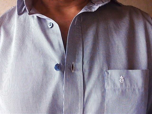PlaisirsPourTous lleva una camisa de manga larga a rayas azules con un bolsillo en el pecho, que deja ver un poco de su piel morena y un solo botón. Es algo elegante..